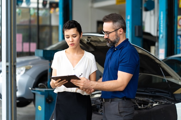 Concepto de seguro de automóvil. El agente de seguros examina el coche dañado con la clienta y escribe la información en el formulario de informe de reclamación.