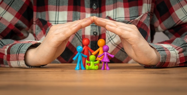 Concepto de seguro familiar con figuras familiares coloridas cubiertas por las manos en una pancarta de mesa de madera Foto de seguridad y apoyo
