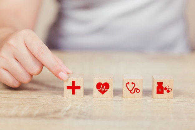 Concepto de seguro de salud, mano arreglando el apilamiento de bloques de madera con icono de atención médica.