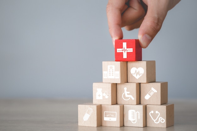 Concepto de seguro de salud, mano arreglando el apilamiento de bloques de madera con el icono de atención médica.