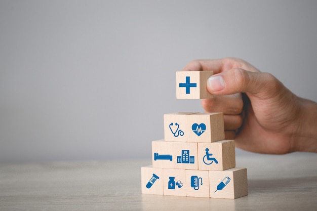 Foto concepto de seguro de salud, mano arreglando apilamiento de bloques de madera con icono de salud médica.