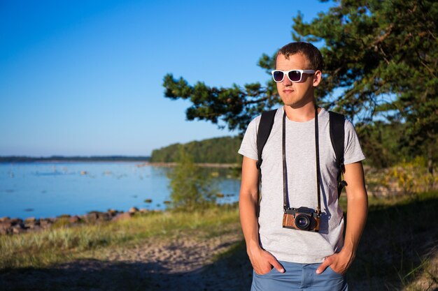 Concepto de senderismo - hombre guapo en anteojos con mochila y cámara retro en la playa