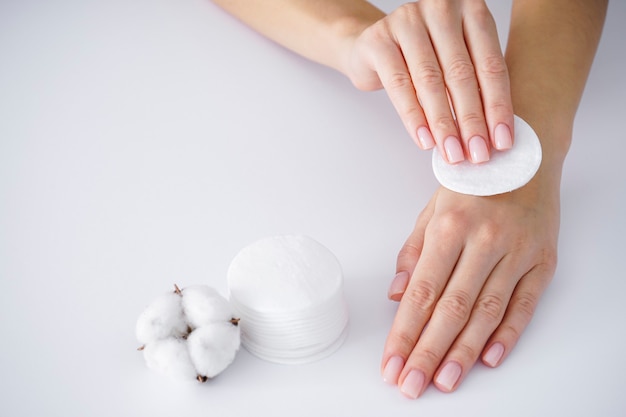 Concepto de spa. Manos de una mujer joven con un disco de algodón, flor de algodón blanco sobre un fondo blanco. Manicura femenina. Flor de algodón.