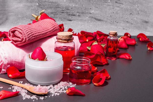 Concepto de spa natural con pétalos de rosas frescas. Sal de rosa, aceite esencial, toallas suaves. Luz dura moderna, sombra oscura. Fondo de hormigón de piedra negra, espacio de copia