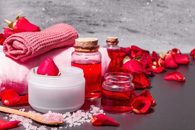 Concepto de spa natural con pétalos de rosas frescas. Sal de rosa, aceite esencial, toallas suaves. Luz dura moderna, sombra oscura. Fondo de hormigón de piedra negra, espacio de copia