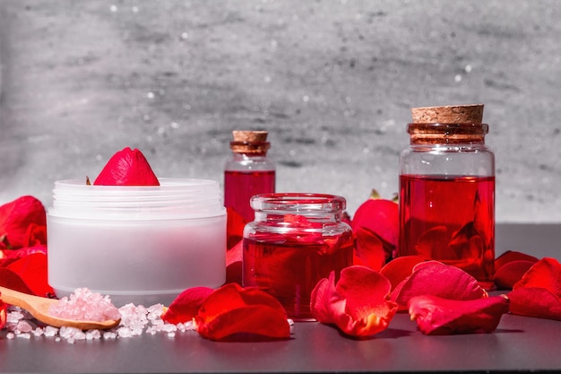 Concepto de spa natural con pétalos de rosas frescas. Sal de rosa, aceite esencial, toallas suaves. Luz dura moderna, sombra oscura. Fondo de hormigón de piedra negra, espacio de copia