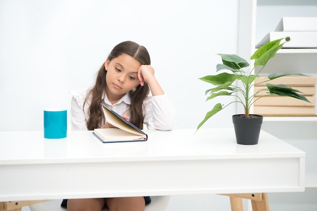 Concepto de tarea. La chica hace la tarea aburrida. Niño pequeño cansado de hacer la tarea en el escritorio. Asignación de tareas.