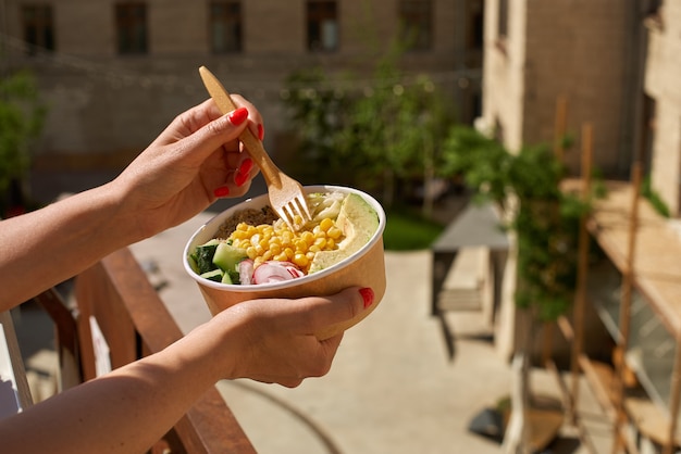 Concepto de tazón de fuente del almuerzo vegano saludable en manos femeninas en la calle. Ensalada de aguacate y quinua. entrega de comida, comida para llevar.