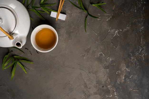 Concepto de té asiático, taza de té y tetera rodeada de té verde hojas secas vista desde arriba