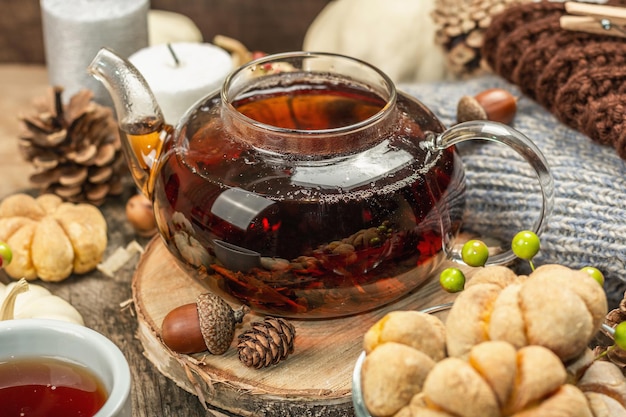 Concepto de té de otoño. Galletas con puré de calabaza, té negro en una tetera de cristal, decoración otoñal. Corona, velas, un suéter acogedor. Fondo de madera vieja, cerrar