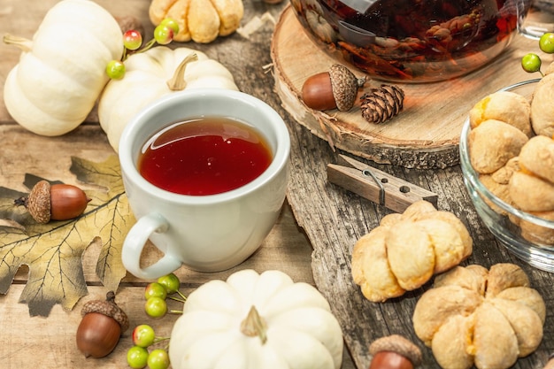 Concepto de té de otoño. Galletas con puré de calabaza, té negro en una tetera de cristal, decoración otoñal. Corona, velas, un suéter acogedor. Fondo de madera vieja, cerrar