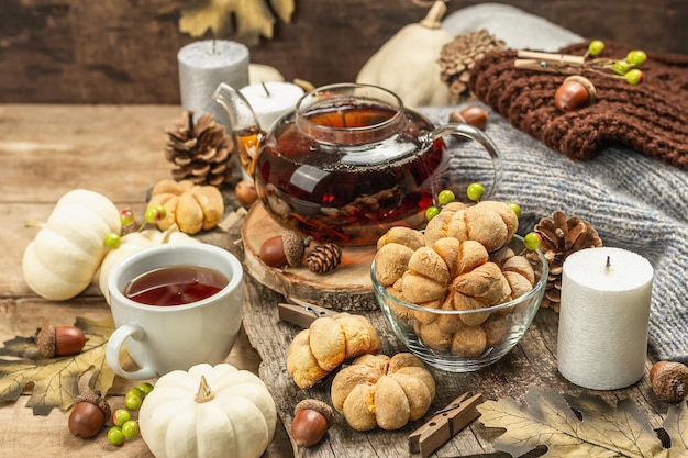 Concepto de té de otoño. Galletas con puré de calabaza, té negro en una tetera de cristal, decoración otoñal. Corona, velas, un suéter acogedor. Fondo de madera vieja, espacio de copia