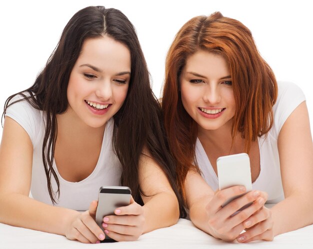 Foto concepto de tecnología, amistad y personas: dos adolescentes sonrientes con teléfonos inteligentes