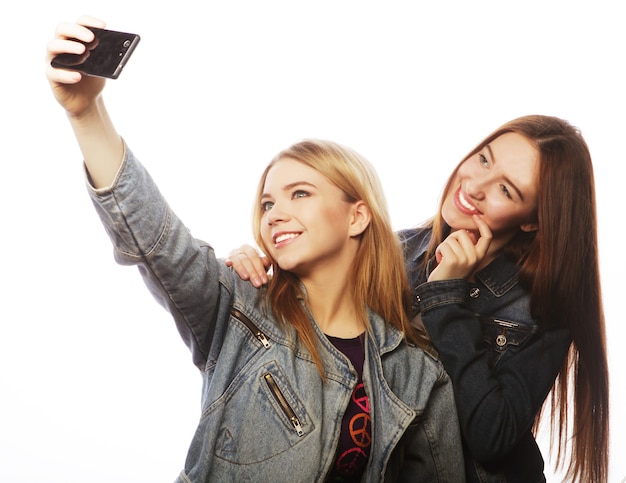 Concepto de tecnología, amistad y personas: dos adolescentes sonrientes tomando fotografías con la cámara del teléfono inteligente