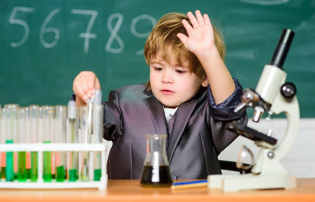 Concepto de tecnología y ciencia Niño estudia biología y química en la escuela Educación escolar Explora moléculas biológicas Niño genio bebé Niño cerca de microscopio y tubos de ensayo en el aula de la escuela