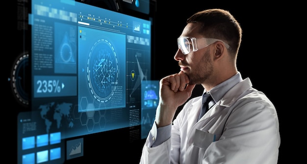concepto de tecnología, ciencia y personas: médico o científico masculino con bata blanca y gafas de seguridad mirando la pantalla virtual sobre fondo negro