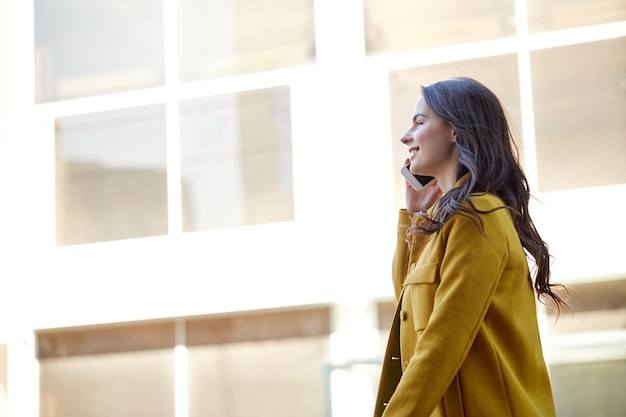 concepto de tecnología, comunicación y personas - mujer joven sonriente o adolescente llamando a un teléfono inteligente y caminando por la calle de la ciudad