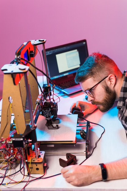 Concepto de tecnología e ingeniería: un ingeniero que trabaja de noche en el laboratorio, ajusta los componentes de una impresora 3D.