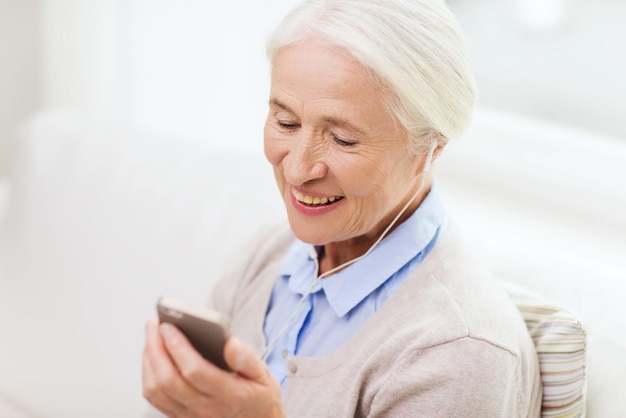 concepto de tecnología, edad y personas - anciana feliz con smartphone y auriculares escuchando música en casa