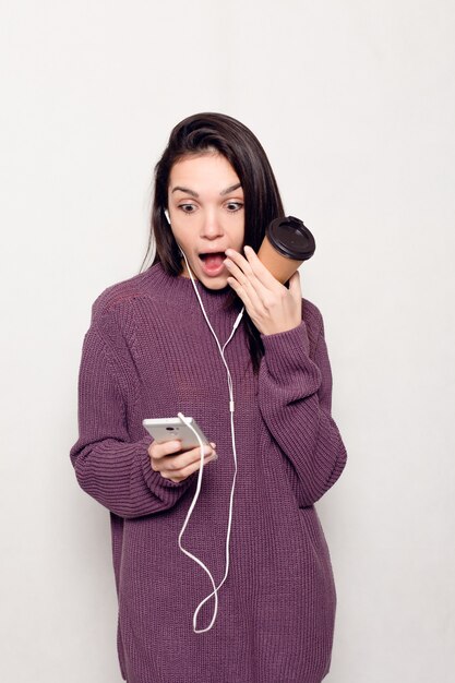 Concepto de tecnología, estilo de vida, adicción a internet y personas - mujer hermosa joven con teléfono inteligente. Mujer atractiva feliz y sonriente mirando el teléfono móvil. Pared gris al fondo.