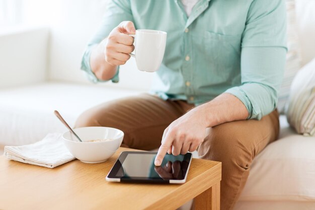 concepto de tecnología, hogar, bebidas, comida y estilo de vida: cierre de un hombre con una tableta y una taza de café desayunando en casa