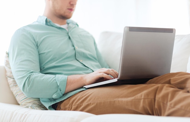 concepto de tecnología, hogar y estilo de vida: cierre de un hombre que trabaja con una computadora portátil y se sienta en un sofá en casa