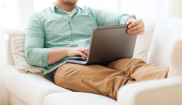 concepto de tecnología, hogar y estilo de vida: cierre de un hombre que trabaja con una computadora portátil y se sienta en un sofá en casa