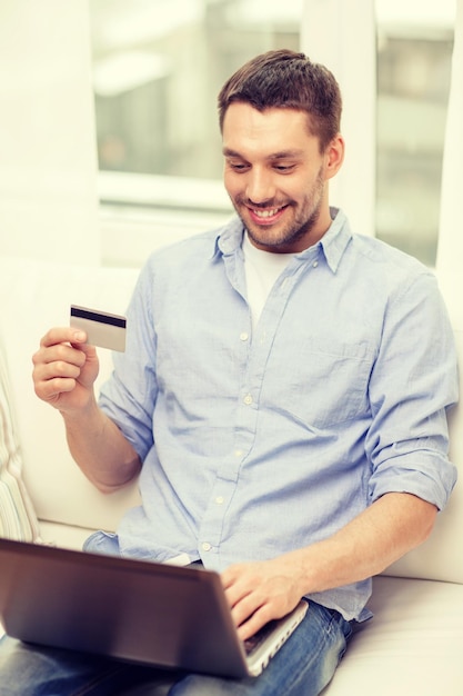 concepto de tecnología, hogar y estilo de vida - hombre sonriente trabajando con laptop y tarjeta de crédito en casa