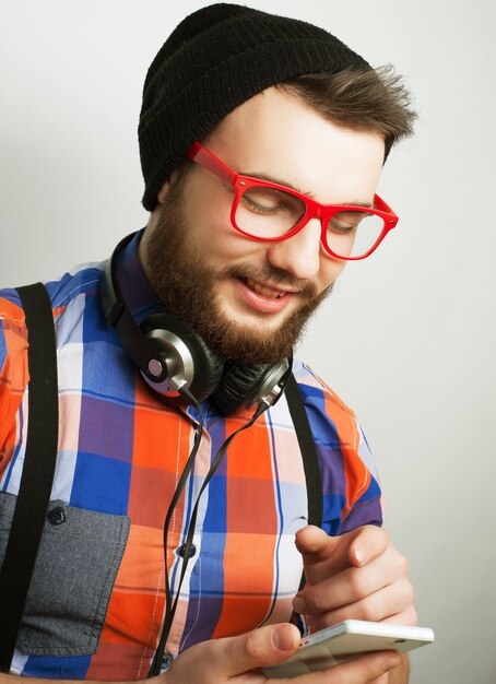 Concepto de tecnología, internet, emocional y personas: joven barbudo con móvil sobre fondo gris. Estilo hipster. Tonificación de moda especial.