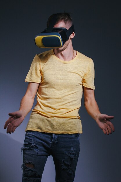 Concepto de tecnología, juegos, entretenimiento y personas - hombre joven con casco de realidad virtual o gafas 3d. Foto de estudio, fondo gris.
