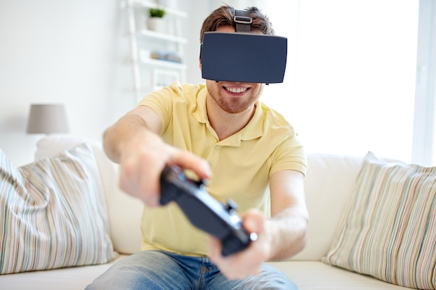 Concepto de tecnología, juegos, entretenimiento y personas: joven feliz con auriculares de realidad virtual o gafas 3d con gamepad controlador jugando videojuegos de carreras en casa