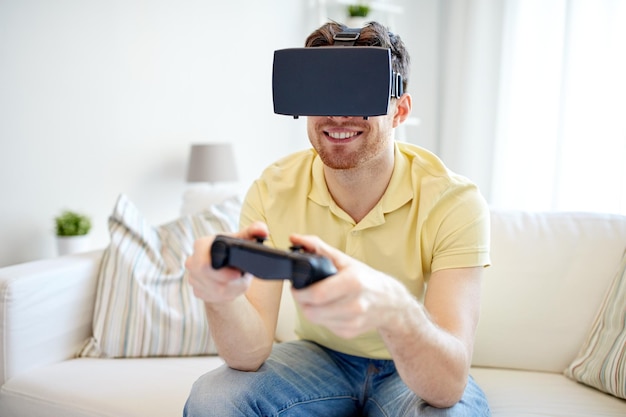 concepto de tecnología, juegos, entretenimiento y personas - joven feliz con auriculares de realidad virtual o gafas 3d jugando videojuegos con gamepad controlador en casa