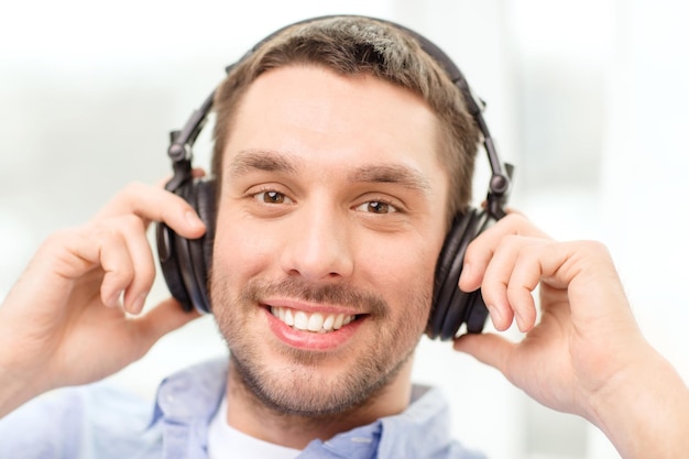 concepto de tecnología, música y felicidad - joven sonriente con auriculares en casa