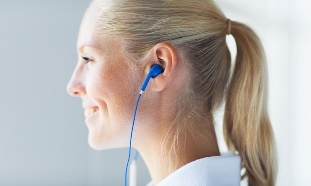 concepto de tecnología, música y personas - cerca de una mujer sonriente feliz con auriculares en casa