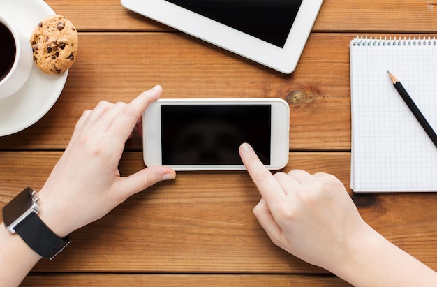 concepto de tecnología, negocios, comunicación, personas y publicidad: cierre de una mujer con una pantalla de smartphone en blanco y una taza de café en una mesa de madera