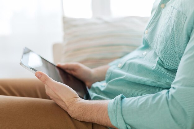 concepto de tecnología, ocio, estilo de vida y aprendizaje a distancia: cierre de un hombre que trabaja con una computadora de tableta sentado en un sofá en casa