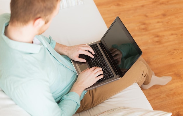 concepto de tecnología, ocio, publicidad y estilo de vida: cierre de un hombre que trabaja con una computadora portátil y se sienta en un sofá en casa