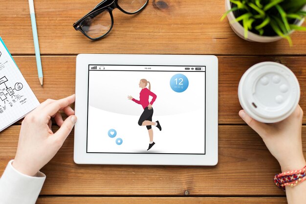 concepto de tecnología, personas y deporte - cierre de mujer con aplicación de fitness en la pantalla de la computadora de tablet pc y café en la mesa de madera