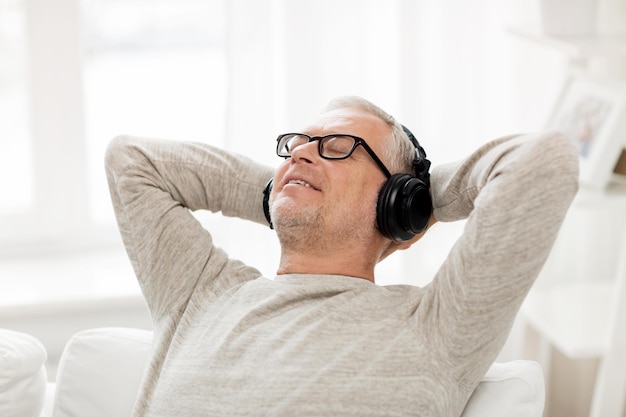 concepto de tecnología, personas y estilo de vida - anciano feliz con auriculares escuchando música en casa