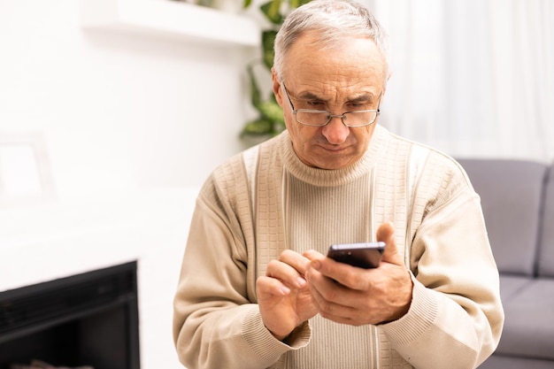 Concepto de tecnología, personas, estilo de vida y comunicación: hombre mayor feliz marcando el número de teléfono y enviando mensajes de texto en el teléfono inteligente en casa.