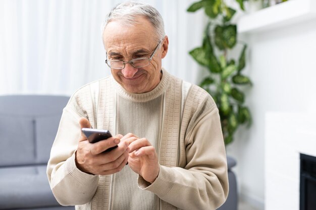 Concepto de tecnología, personas, estilo de vida y comunicación: hombre mayor feliz marcando el número de teléfono y enviando mensajes de texto en el teléfono inteligente en casa.