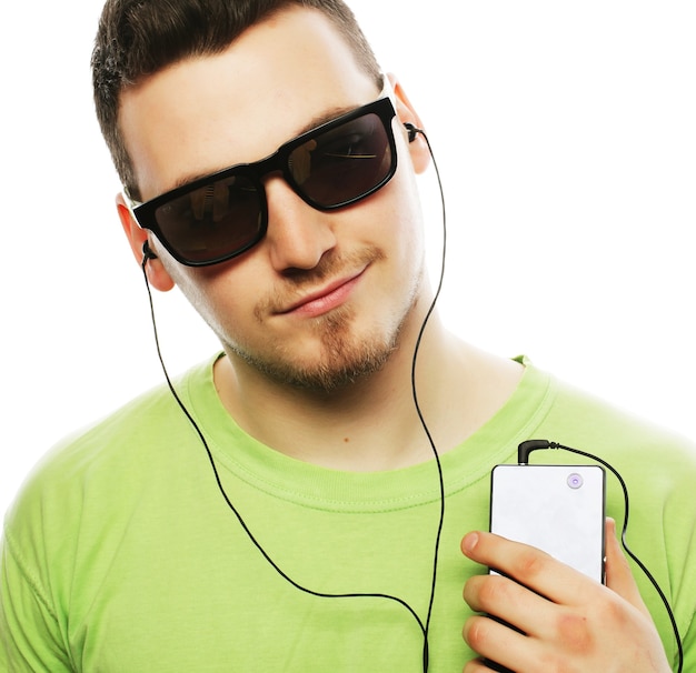 Concepto de tecnología y personas - hombre joven con camiseta verde escuchando música y usando un teléfono inteligente, aislado en blanco