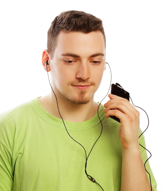 Concepto de tecnología y personas joven con camiseta verde escuchando música y usando un teléfono inteligente aislado en blanco