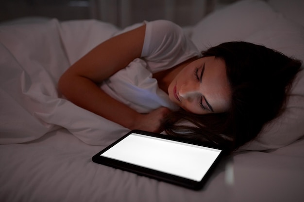 concepto de tecnología y personas: mujer joven con computadora tablet pc durmiendo en la cama en casa por la noche