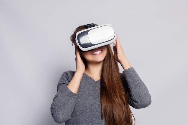 Concepto de tecnología, realidad virtual, entretenimiento y personas - mujer joven feliz con casco de realidad virtual o gafas 3d. Mujer con gafas de realidad virtual. Tiro del estudio, fondo gris