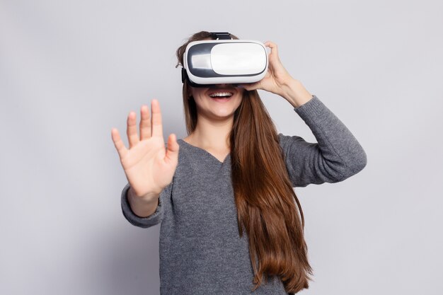 Concepto de tecnología, realidad virtual, entretenimiento y personas - mujer joven feliz con casco de realidad virtual o gafas 3d. Mujer con gafas de realidad virtual. Tiro del estudio, fondo gris