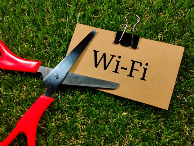 Concepto de tecnología Texto WIFI escrito en tarjeta marrón con tijeras sobre fondo de hierba