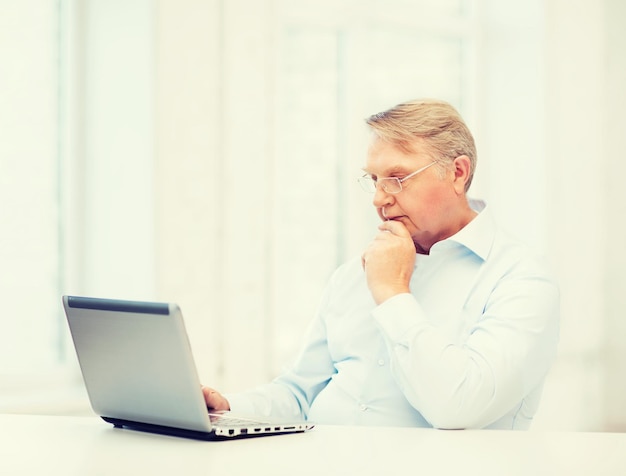 concepto de tecnología, vejez y estilo de vida - anciano en anteojos trabajando con computadora portátil en casa