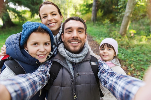 Foto concepto de tecnología, viajes, turismo, caminatas y personas - familia feliz con mochilas tomando selfie y caminatas