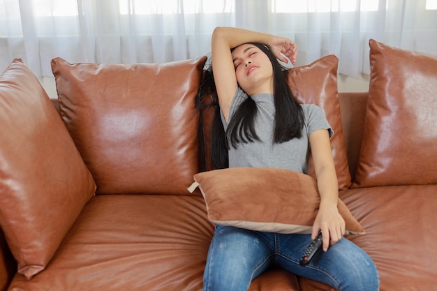 Concepto de televisión y felicidad. Hermosa mujer asiática en dormir informal en el sofá en la sala de estar, sosteniendo el control remoto de la televisión y durmiendo mientras ve la televisión con cara sonriente feliz. Concepto de estilo de vida.